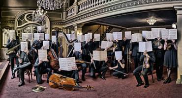 image du musiciens de l'orchetsre visages cachés par une partition ouverte