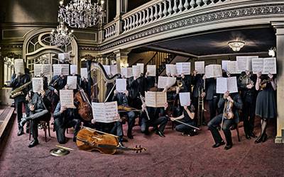 image du musiciens de l'orchetsre visages cachés par une partition ouverte